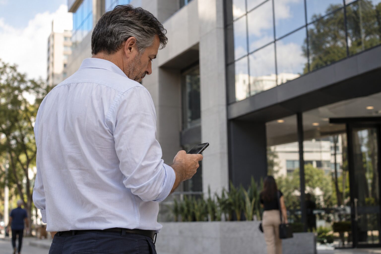 Empresário na calçada conferindo no celular como seu escritório aparece para quem o encontra pela busca, em frente ao prédio comercial.