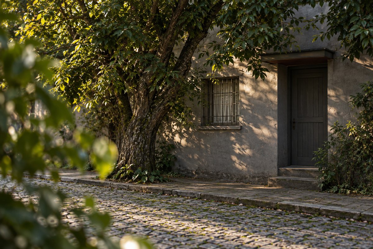 Entrada discreta de uma pequena empresa numa rua de paralelepípedo, meio escondida atrás de uma árvore, sem placa à vista